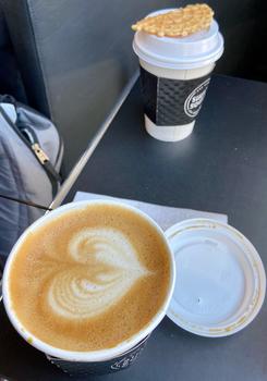 Two coffee cups, one open with latte art of a heart, the other closed with a wafer on top.